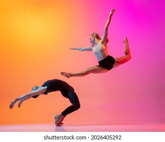 Flying. Two dancers, stylish sportive couple dancing contemporary dance on colorful gradient yellow pink background in neon light. Concept of art, creativity, movement, style and fashion, action.