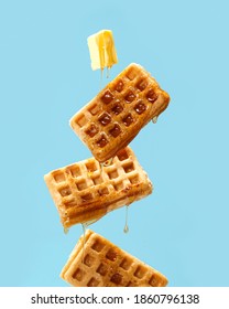 Flying waffles and butter getting dripped with maple syrupo over a light blue background