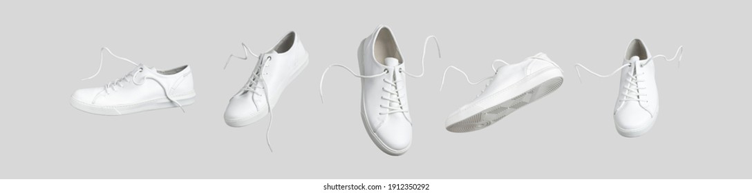 Fliegende weiße Lederfrauenturnschuhe einzeln auf grauem Hintergrund, verschieden. Modische, stilvolle Sportschuhe. Kreatives minimalistisches Layout mit Schuhen. Werbung für Schuhgeschäfte, Blog