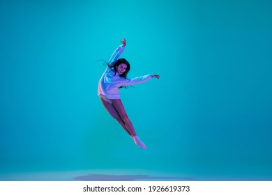 Flying. Young and graceful ballet dancer isolated on blue studio background in neon light. Art, motion, action, flexibility, inspiration concept. Flexible caucasian ballet dancer, moves in glow.