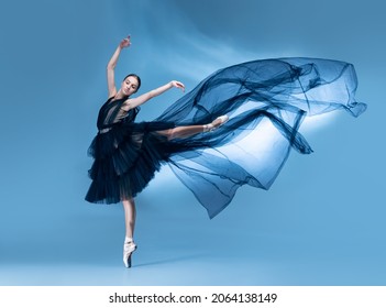 Flying. Young and graceful ballet dancer in black stage outfit, dress dancing isolated on white blue studio background in neon light. Art, motion, action, beuaty, flexibility, inspiration concept.