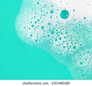 Foam with bubbles. Soap sud on turquoise background. Detergent in water. Abstract soapy texture. Flat lay.