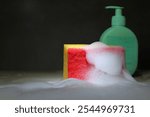 Foam dishwashing sponge in soap suds with rubber gloves on kitchen counter for cleaning and washing design.