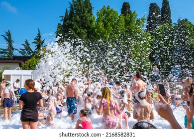 Foam Party Disco At Summer Sunny Day. Happy And Joyful Kids And People Dancing In Swimsuits Near Water Pool. Seaside Vacation And Hotel Resort Concept. Sochi, Russia - 01.06.2022