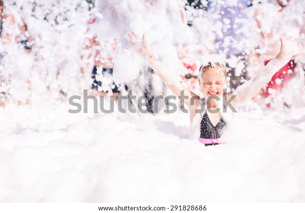 Foam Party on the beach. Cute little girl having\
fun and dancing.
