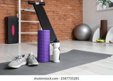 Rodillo de la espuma con las zapatillas de deporte y la botella de agua en el gimnasio de la estera