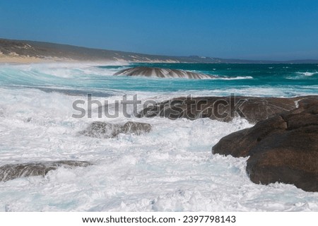 Foam and spray from braking waves in the foreground with the coastline and blue summer sky in the background