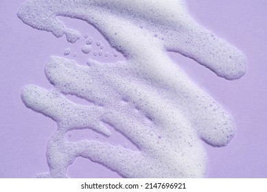 Foam swatch on a lilac background. Soapy liquid texture with bubbles. Natural sunshine and shadows. Skin care cleansing cosmetic in top view. - Shutterstock ID 2147696921