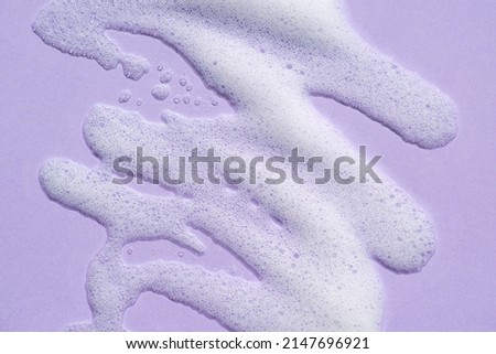 Foam swatch on a lilac background. Soapy liquid texture with bubbles. Natural sunshine and shadows. Skin care cleansing cosmetic in top view.