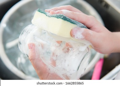 Foamy Hands Of Child Wash & Clean Glass Jars In Kitchen Sink With Sponge. Daily Chores Improve Life Skills, Growth Mindset, Self-confidence And Responsibility. Montessori Child Development Concept.