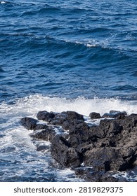 Foamy ocean waves crash against dark volcanic rocks along the coast.