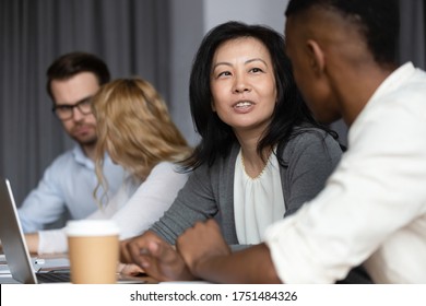 Focus to asian ethnicity middle-aged woman mentor more experienced worker teach African guy millennial intern, diverse staff members sitting in co-working shared room working on common project concept - Powered by Shutterstock