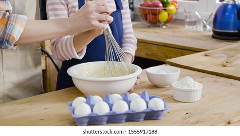 focus close up photo mom holding kid hands whipping butter and flour in bowl with whisk on wooden table. Making apple pie easter cake or cookies on mothers day. parent and child diy by carton of egg