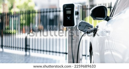 Focus closeup electric vehicle plugged in with EV charger device from blurred background of public charging station powered by renewable clean energy for progressive eco-friendly car concept.