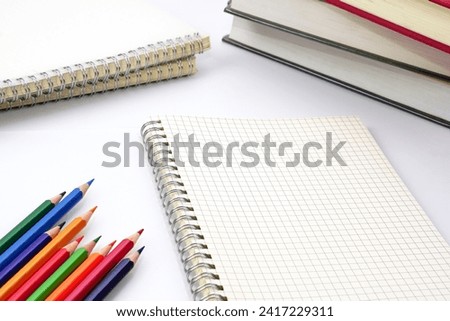 Focus of colored pencils or pastel lined up placed on graph book and blur stack of books on white background. Learning, study and presentation concept.