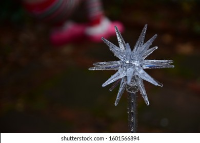 In Focus In The Foreground Is A Star-shaped Garden Ornament Glazed With Rain Water, And Blurred In The Background Are The Pink Shoes Of A Child On A Backyard Swing Set