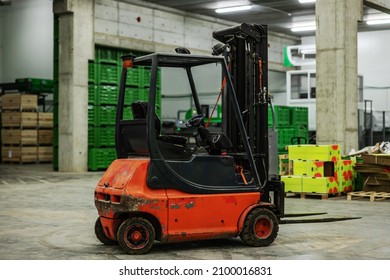 In Focus Forklift In The Warehouse. The Old Rusty Forklift Is In An Empty Warehouse With No People. In The Background Are Boxes And Pallets For Packing Fresh Fruits And Vegetables. Transportation