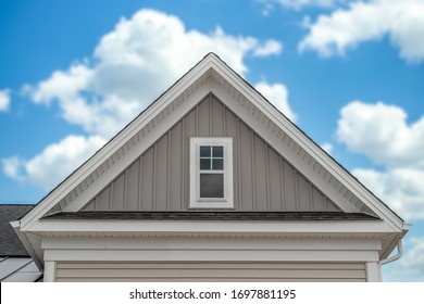 In Focus Gable On A Newly Built Single Family House With White Fascia, Common Rafter, Soffit, Vertical Vinyl Siding, Decorative White Trim, Rectangular Double Sash Attic Window Blurred Cloudy Sky