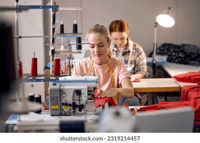 focus on adorable caucasian blonde lady using sewing machine. happy women working as seamstress in clothing factory, clothing production concept. dressmaking, tailoring in workshop