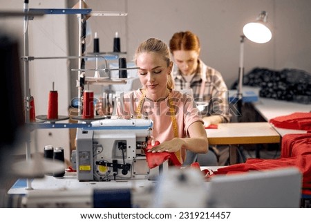 focus on adorable caucasian blonde lady using sewing machine. happy women working as seamstress in clothing factory, clothing production concept. dressmaking, tailoring in workshop