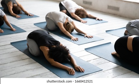 Focus On African Ethnicity Woman With Group Of Multi Ethnic People Lying On Mats Perform Beginner Yoga Child Pose, Stretches Low Back Muscles, Improve Inner Balance, Mental And Body Relaxation Concept