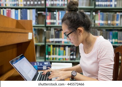 Focus On Asian Student Concentrating On Study In Library With Stress. Young Adult Woman Wear Glass Sit In Front Of Laptop Computer Alone.