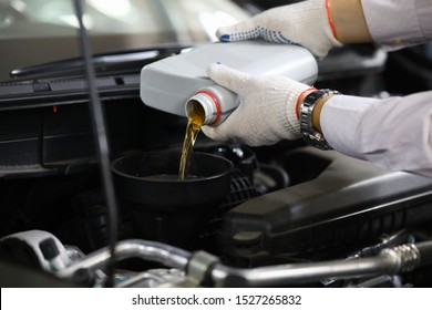 Focus on auto mechanic in gloves replacing and pouring fresh oil into engine at automobile service station. Vehicle inspection concept. Blurred background