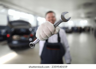 Focus on automechanic male hand holding important tool and showing utility for fixing car at camera. Machinery checkup and service station concept. Blurred background - Powered by Shutterstock