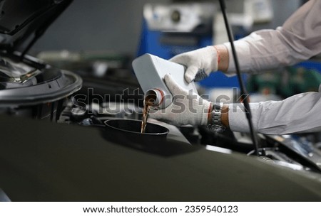 Focus on automechanic male hands in white gloves using canister of machinery liquid and precisely pouring under hood of sportcar. Automotive checkup concept