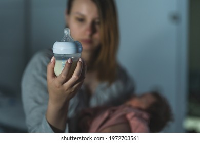 Focus on bottle milk instant formula mother checking content while holding her newborn baby sitting on bed at night in dark room at home - Powered by Shutterstock