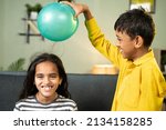 Focus on boy, Kids enjoys static cling experiment by playing while rubbing ballon to hair and hairs attracted to ballon - conept of excitement and home science experiment.