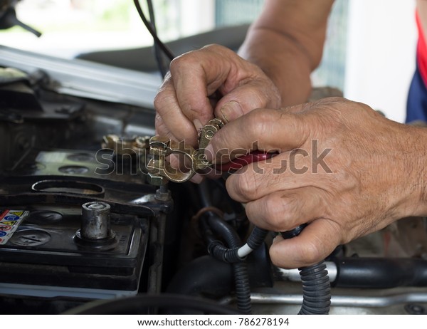 focus on brass battery terminal in old man\'s\
hands doing fix car\
battery