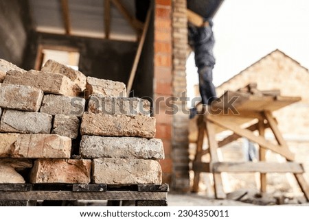 Focus on a bricks with housebuilder building a house in a blurry background.