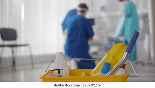 Focus On Bucket With Detergents And Nurse Team Cleaning Ward In Hospital On Blurred Background. Medical Staff Disinfecting Empty Recovery Room In Modern Clinic