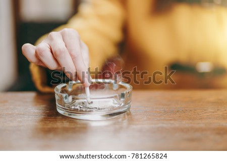 Focus on caucasian young woman hand putting out cigarette on glass ashtray on wooden table, cigarette butt, smoking is dying. Quit smoking. Health concept. Close up photo