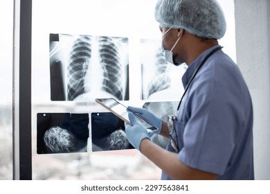 Focus on chest X-ray examination studied by multiracial healthcare practitioner in protective garment using tablet with stylus pen. Male radiologist identifying mass in left lung using technologies. - Powered by Shutterstock