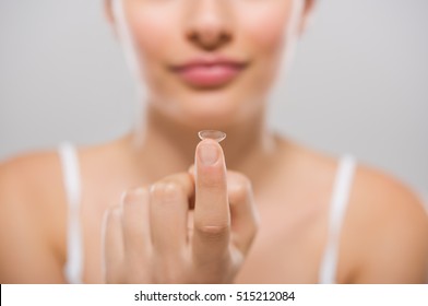 Focus On Contact Lens On Finger Of Young Woman. Young Woman Holding Contact Lens On Finger In Front Of Her Face. Woman Holding Contact Lens On Grey Background. Eyesight And Eyecare Concept.
