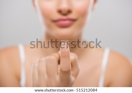 Focus on contact lens on finger of young woman. Young woman holding contact lens on finger in front of her face. Woman holding contact lens on grey background. Eyesight and eyecare concept.
