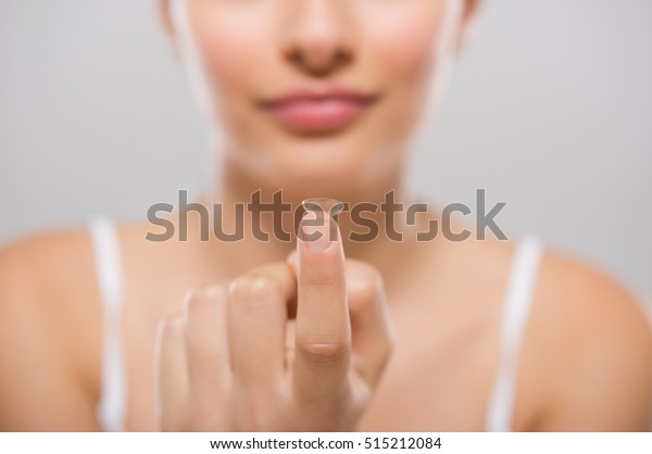 Focus on contact lens on finger of young\
woman. Young woman holding contact lens on finger in front of her\
face. Woman holding contact lens on grey background. Eyesight and\
eyecare concept.\
