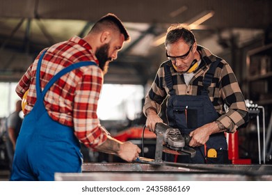 Focus on a craftsman with safety goggles holding a grinder in his hands while his colleague is marking the metal ingot with his pen. Working together as a team in a dangerous environment. Copy space. - Powered by Shutterstock