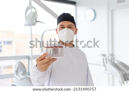 Focus on a dentist's hand holding a dental implant model while his face is out of focus in the background. Selective focus