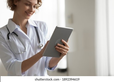 Focus on digital computer tablet in young female doctor hands, copy space. Smiling pleasant general practitioner using modern electronic gadget in clinic office, giving medical consultation online.