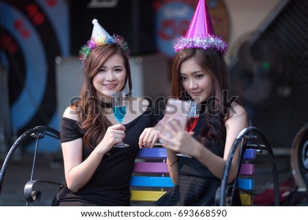 Focus on face of Beautiful girls holding colorful cocktail with Funny Happy taking selfie in a bar with smart phone. Cheerful friends girls partying in club at night on dark background.