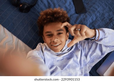 Focus on face of cheerful African American teenage boy looking at camera with smile while relaxing on bed at leisure and taking selfie - Shutterstock ID 2293901153
