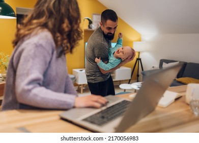 Focus On A Father Playing With His Baby Boy While Mother Is Working On Her Laptop In The Kitchen At Home. Home Lifestyle. Family Time.