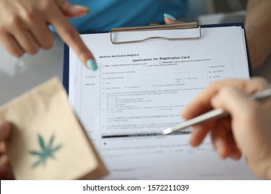 Focus on female hand holding paper folder and pointing for text. Sick patient with paper package with cannabis symbol on it and signing document. Healthcare and medical marijuana concept