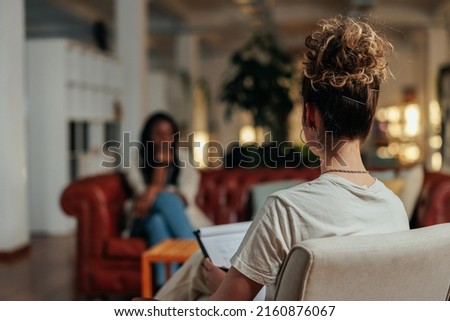 Focus on female psychiatrist writing information of african female patient while sitting on sofa and talking about his illness