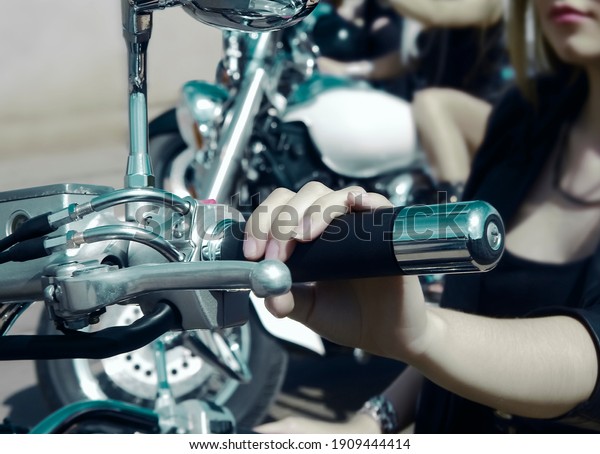 Focus on\
finger.Three Young girls sitting on chopper bike and wear black\
leather dress and stylish sunglasses. 3 Biker Woman on motorcycle\
on green grass medow background. season\
opening