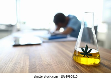 Focus on flask with marijuana label. Man waiting for results of test in laboratory. Workplace of lab with tubes and containers. Medicine and lab researching concept