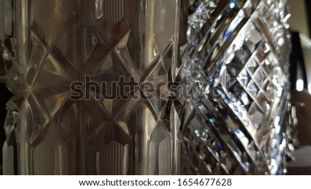 Focus on foreground and blurred background. Abstract ornate crystal backdrop of smooth shiny glass surface closeup. Patterned textures of vintage crystal vases.